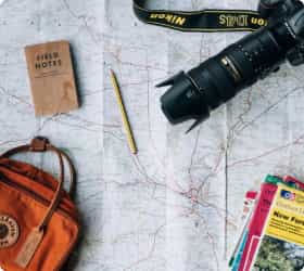 Карта местности, на которой лежит карандаш, фотоаппрат, сумки и блокнот