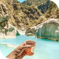 Рука с напитком на фоне гор и лазурно голубой воды