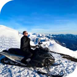 Человек сидит на снегоходе на вершине горы